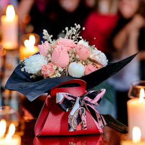 Flower Box dekoracyjna świeca sojowa z małymi różowymi i kremowymi kwiatkami. W czerwonej torebce z kokardą i czarnym akcentem. Z lampkami led.