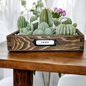 Świeca Kaktusy w Skrzynce z Grysem to bezzapachowa świeca z naturalnego wosku sojowego w drewnianym pojemniku, z kaktusami w odcieniach zieleni i marmurowym grysie.