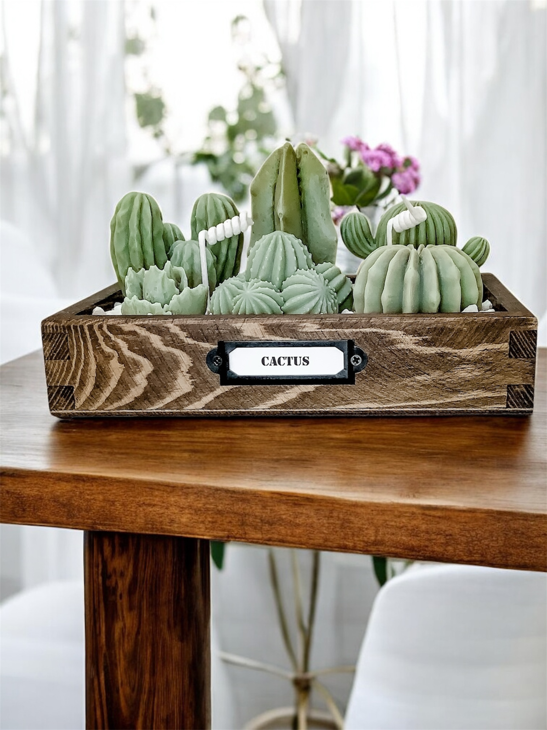 Świeca Kaktusy w Skrzynce z Grysem to bezzapachowa świeca z naturalnego wosku sojowego w drewnianym pojemniku, z kaktusami w odcieniach zieleni i marmurowym grysie.