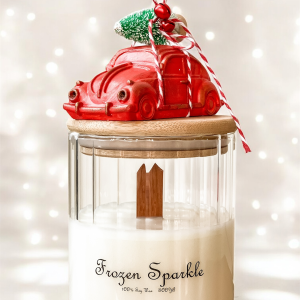Świeca dekoracyjna Frozen Sparkle w szklanym pojemniku z bambusowym wieczkiem. Z dekoracją świąteczną - czerwony garbus z choinką i dzwoneczkiem.