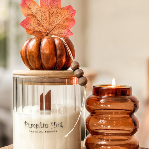 Pumpkin Hug jesienny zestaw - świeca sojowa w szklanym pojemniku z bambusową pokrywką na niej dekoracyjna pomarańczowa dynia. W zestawie pomarańczowy świecznik z grubego szkła.