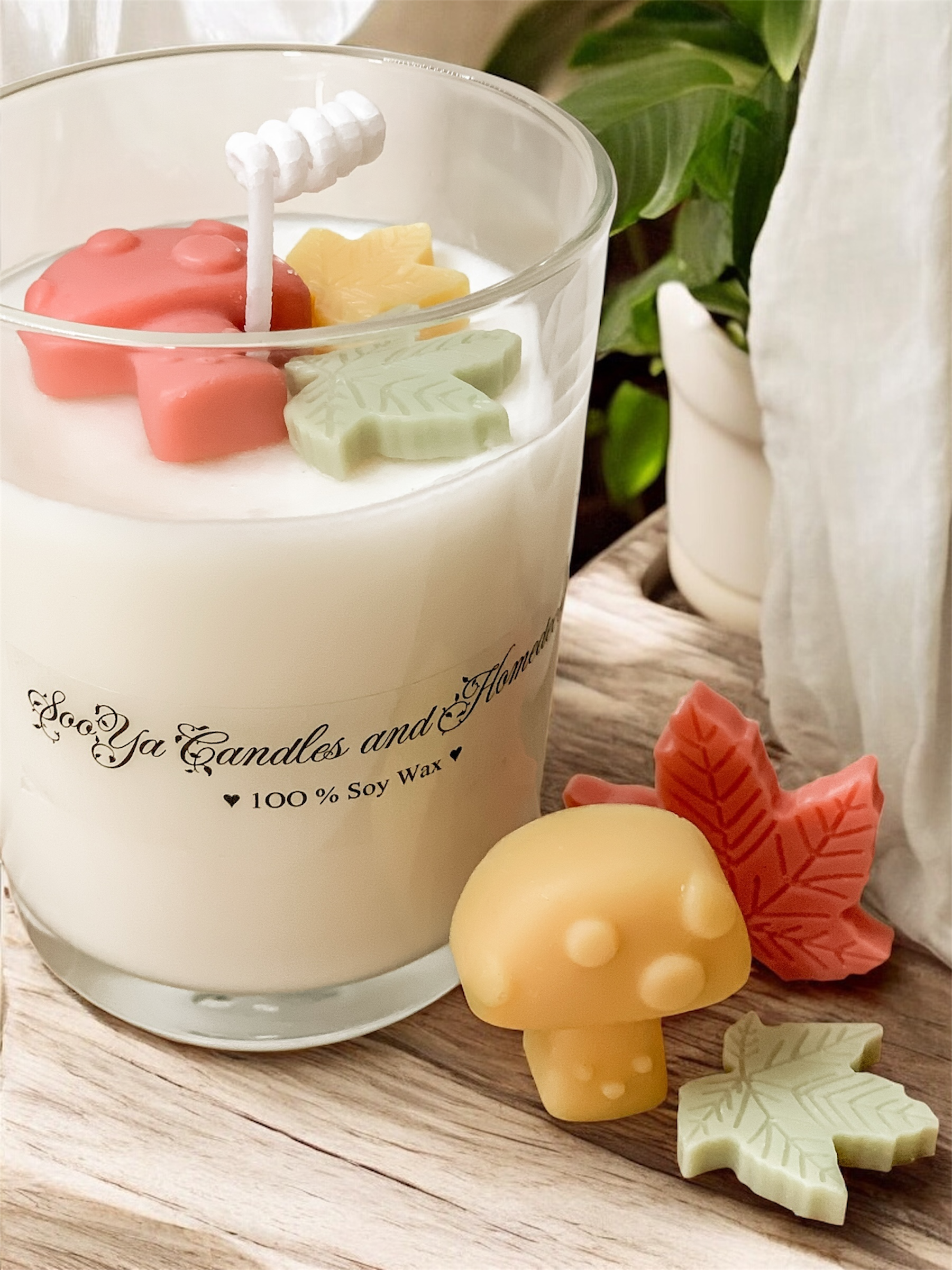 Jesienny zestaw to świeca sojowa w szkle, biały kominek i woski sojowe w kształcie liści i grzybków.