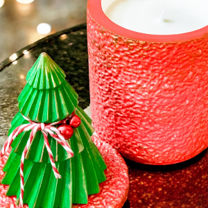 Świąteczna świeca z choinką na pokrywce. Pojemnik w kolorze czerwonym postarzany złotem, choinka zielona z dekoracyjnym czerwonym dzwoneczkiem.