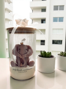 Świeca słonik na szczęście, świeca sojowa w szklanym pojemniku z dekoracyjnym słoniem w koronie. Na pokrywce róża z kokardą.