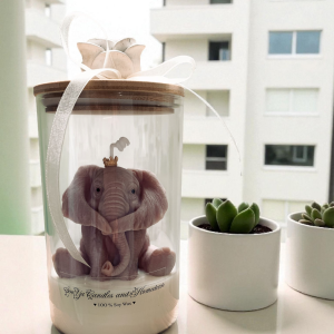 Świeca słonik na szczęście, świeca sojowa w szklanym pojemniku z dekoracyjnym słoniem w koronie. Na pokrywce róża z kokardą.