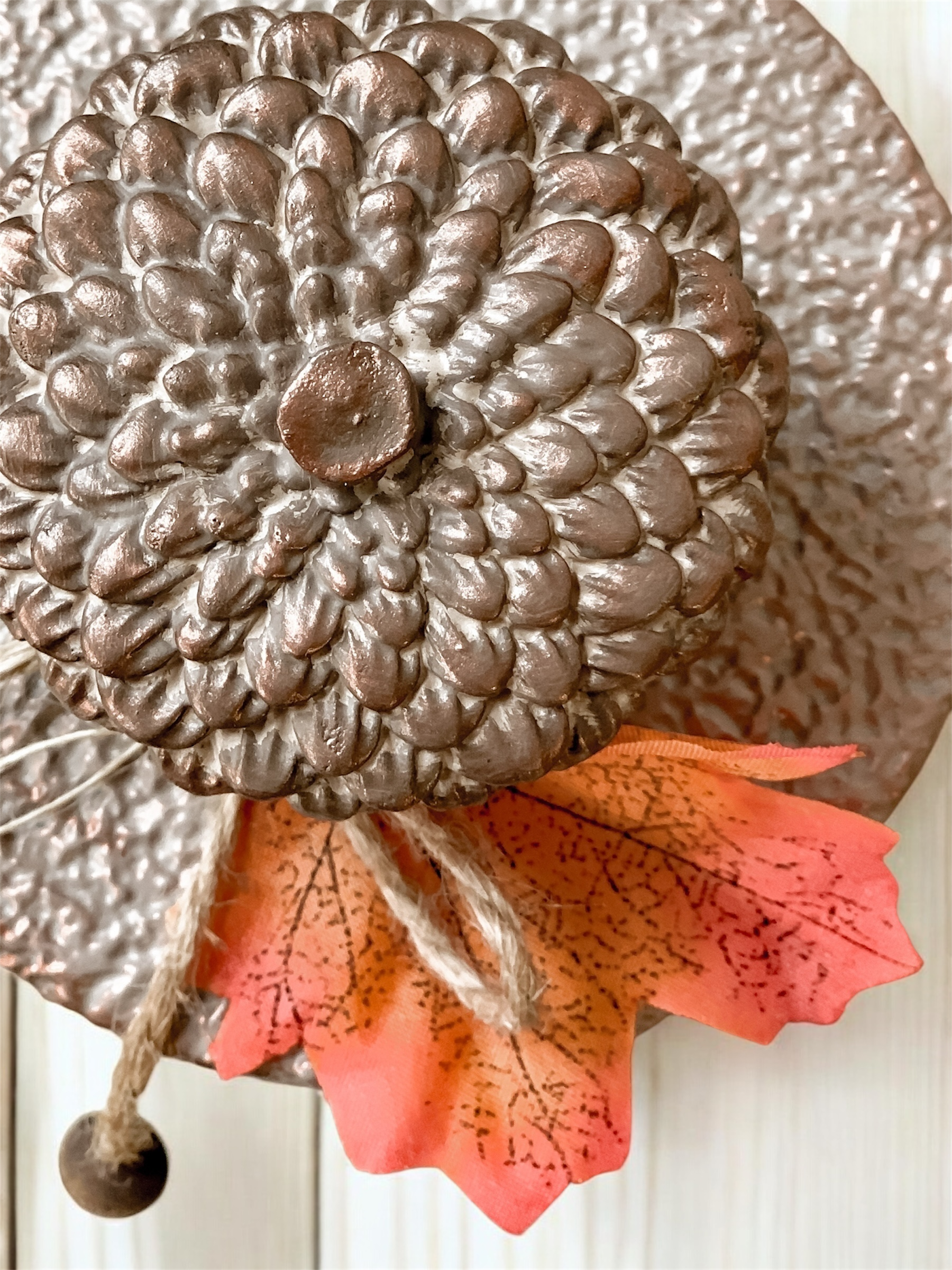 Świeca sojowa Jesienne Żołędzie w brązowym pojemniku z pokrywką, udekorowana dużym brązowym żołędziem i jesiennym liściem, przywiązanym sznurkiem jutowym z drewnianą kulką.