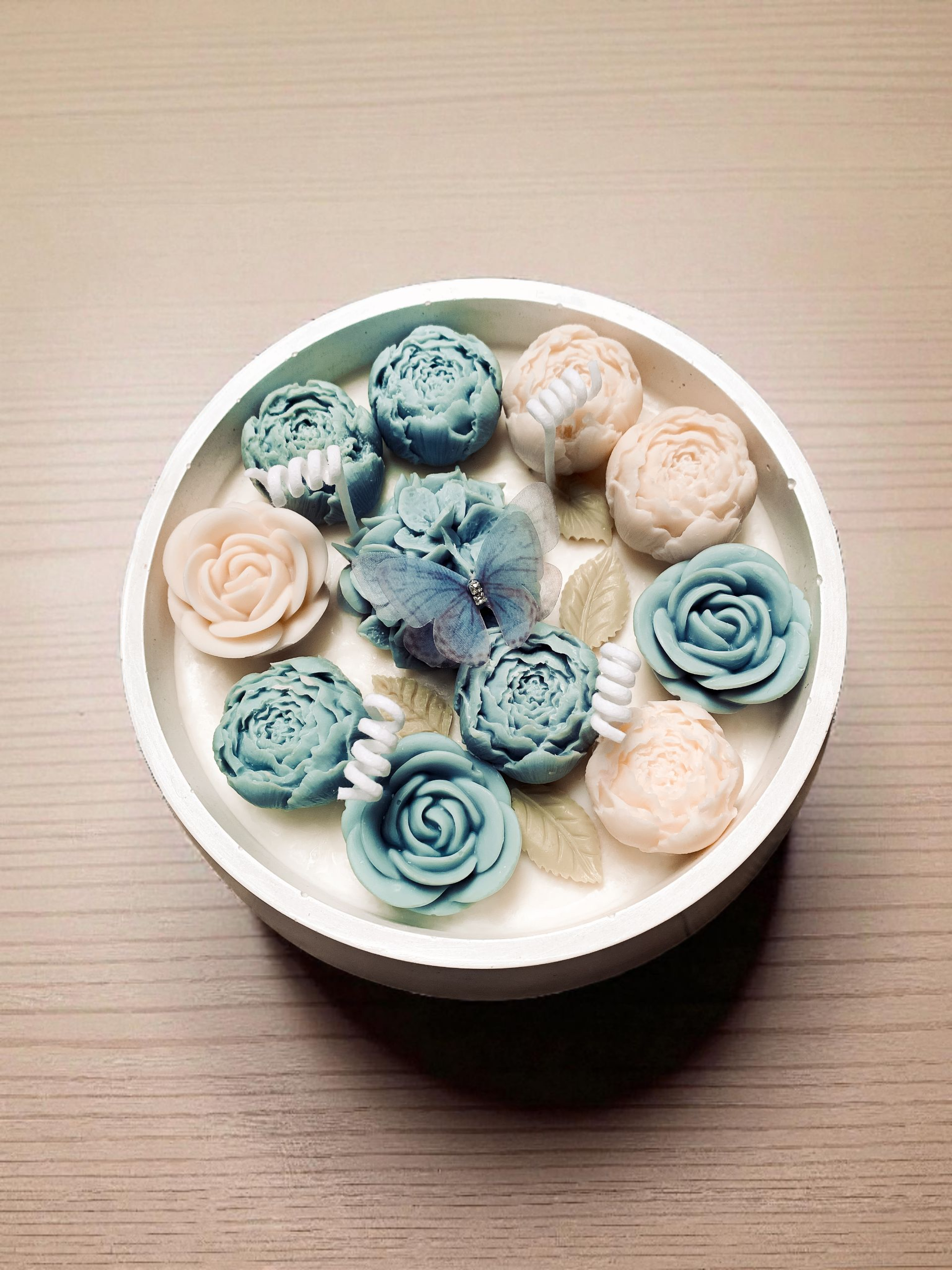 Kwiatowy Ogród Świeca dekoracyjna w pastelowym pojemniku z gipsu, udekorowana kwiatami w odcieniach błękitu i ecru. Na jednym z kwiatów dekoracyjny błękitny motylek.