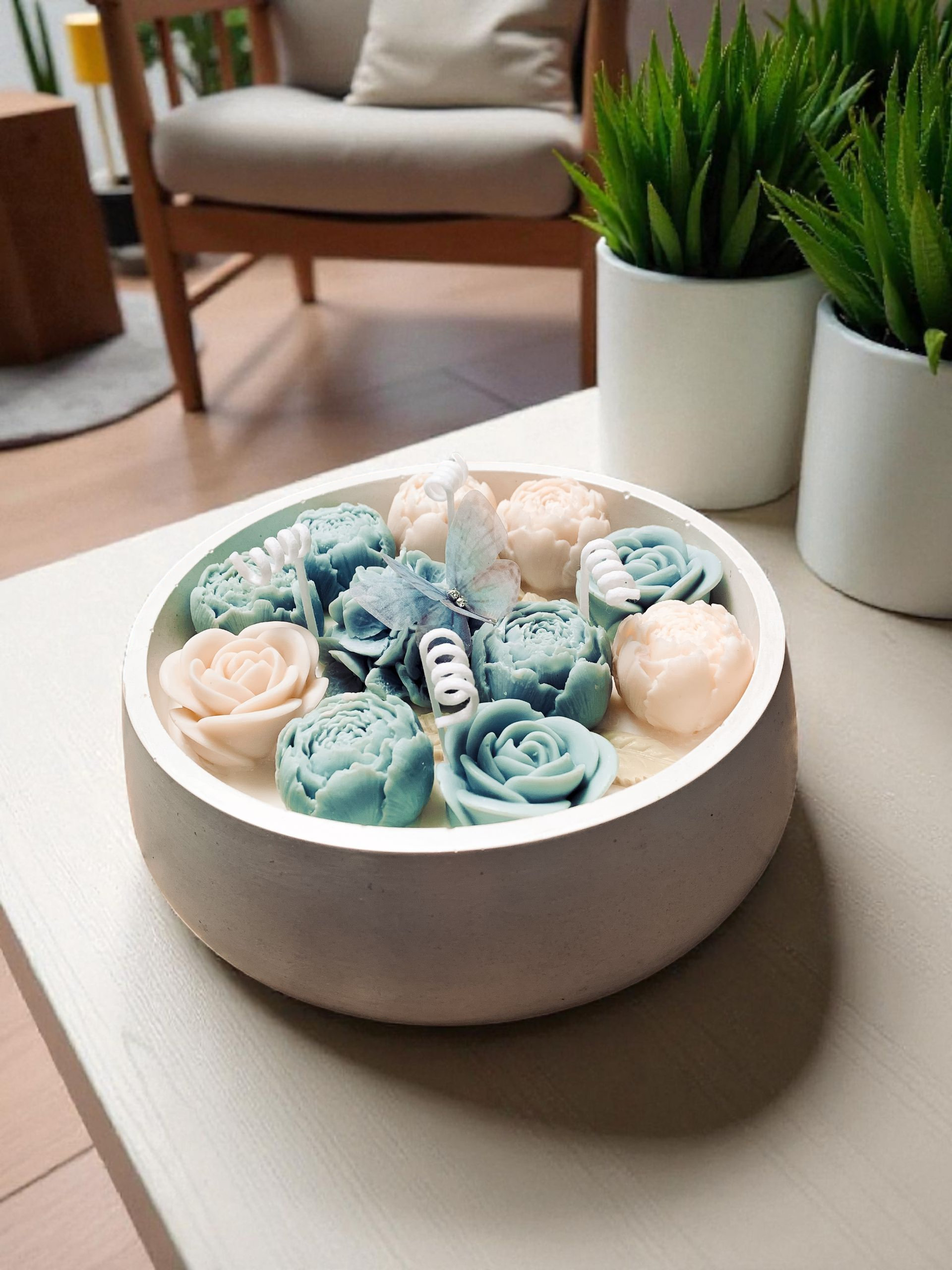 Świeca dekoracyjna Kwiatowy Ogród w okrągłym pastelowym pojemniku z gipsu, udekorowana kwiatami w odcieniach błękitu i ecru. Na jednym z kwiatów dekoracyjny motylek.