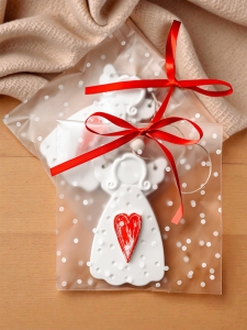 Zawieszka aniołek z sercem – upominek dla gości na wesele, komunię, urodziny, zapakowany w przezroczysty woreczek z czerwoną kokardką.