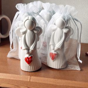 Biały aniołek z sercem – upominki dla gości, zapakowane w białe woreczki z organzy.